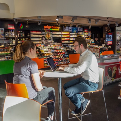 Interviewer zittend aan een tafel in een benzinestation in Zurich, in gesprek met een gebruiker van de POS retail applicatie